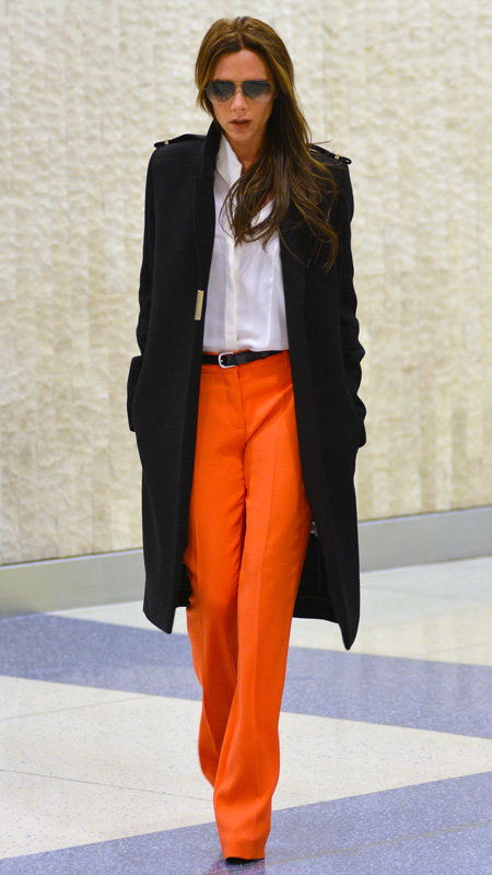 ויקטוריה Beckham wearing orange pants, white top, and black trench coat